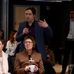 a man is standing and asking some question with mike in one hand