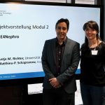 two people man and woman standing infront of screen that shows thier presenattion cover page