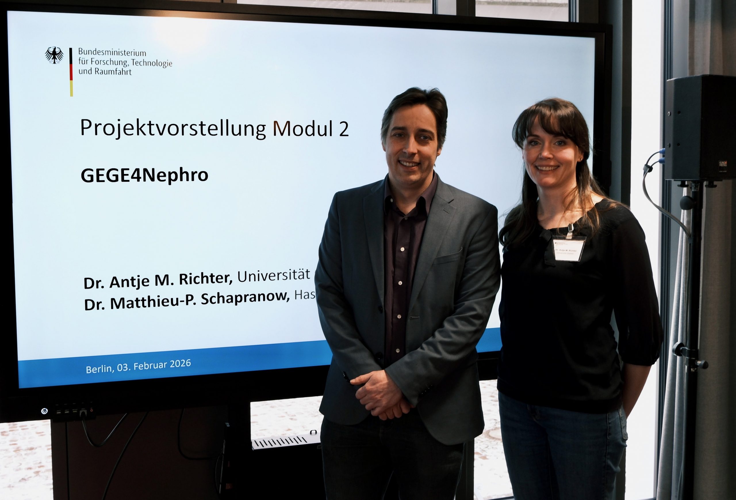 two people man and woman standing infront of screen that shows thier presenattion cover page