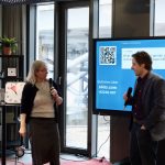 one man and one women holding mikes and talking to each other while there is a screen behind